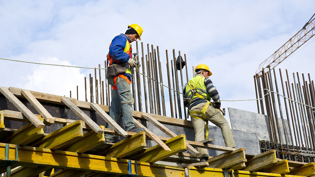 Trabalhadores da área de construção atuando em uma obra, utilizando EPIs
